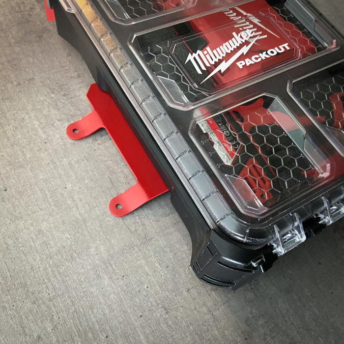 Milwaukee verktygsförvaringslåda väl monterad på röda fästbeslag på grått underlag.