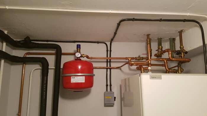 Expansionskärl och ledningar i värmesystem med mätare, ventiler och bergvärmepump märkt "Fighter 1215".