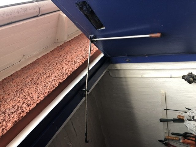 En retro dörrstopp från 50-talet som håller en garagedörr öppen vid 90 grader, monterad på vit vägg och blå dörr.