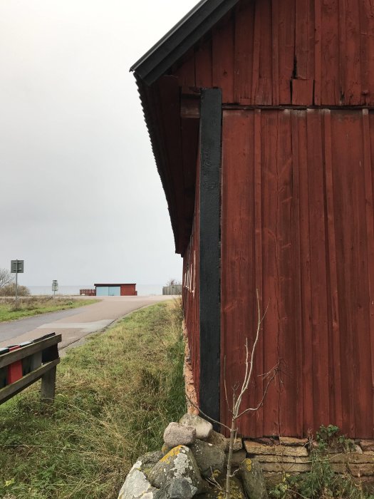 Västlig sida av en röd lada med synligt vindtryck, intill en väg.