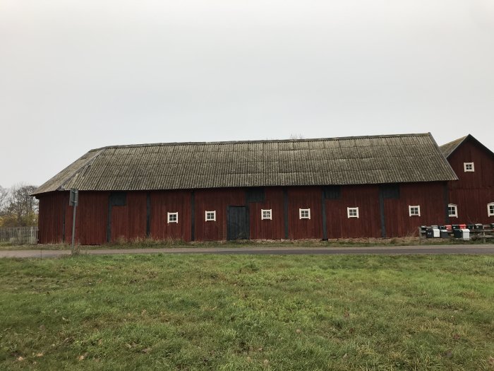 Röd lada med slitet tak och böjd vägg på ena sidan som tecken på vindpåverkan.