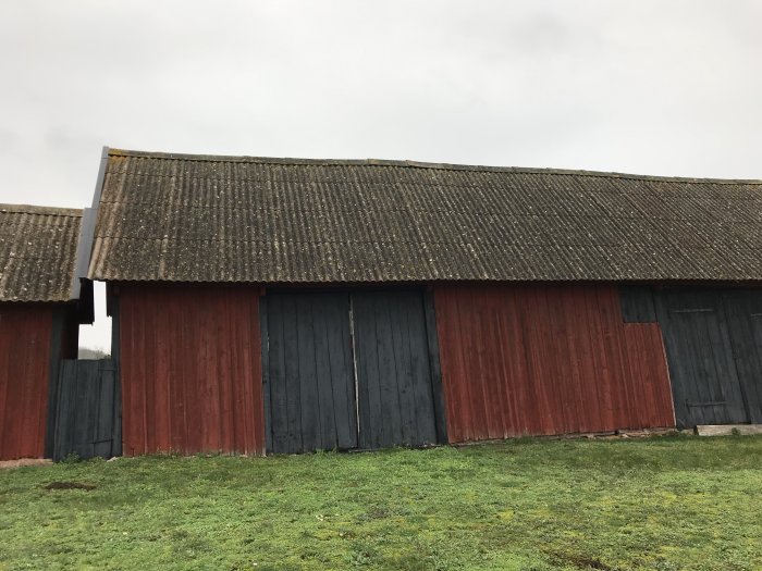 Vindskadad västra sidan på röd lada med böjt tak och flera träportar.