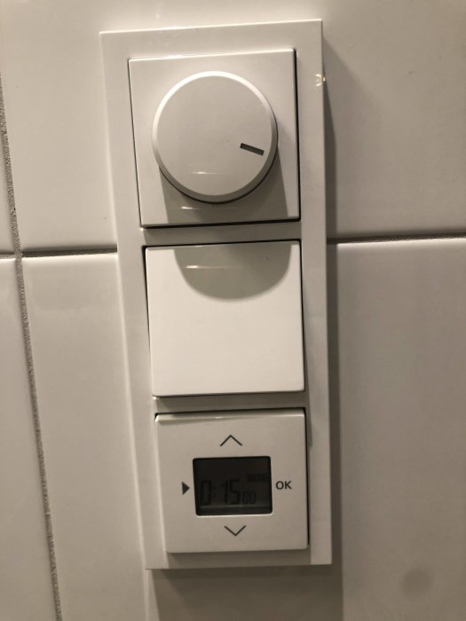 Väggmonterade strömbrytare och timer för golvvärme med display som visar tiden 15:00.