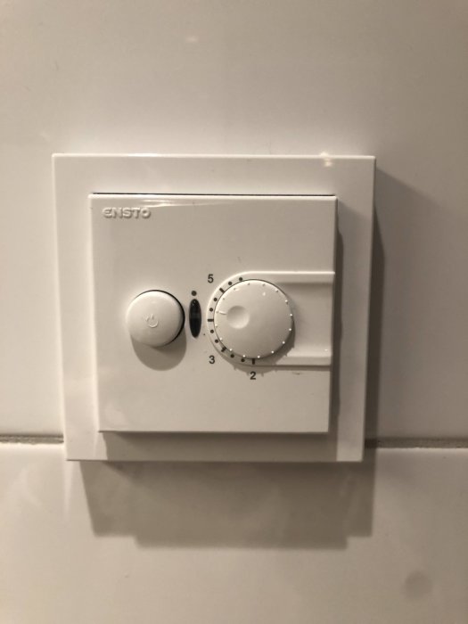 Enso termostat med vridknappar för inställning av golvvärme på en vit kakelvägg.
