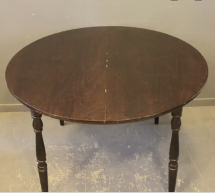 Ett gammalt rundat utdragbart bord med synliga gångjärn och mörk träyta, uppsatt på fyra svarvade ben.