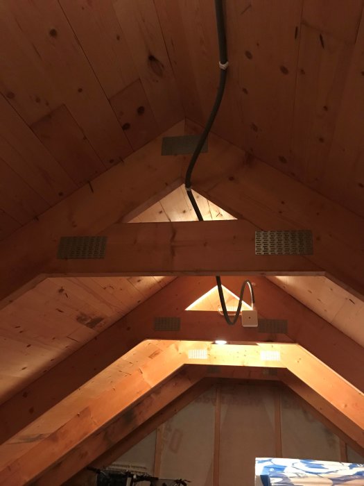 Inredning av garage med träbeklädnad, isolering och synliga takbjälkar med luftspalter.