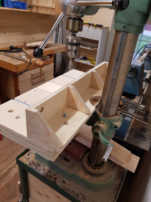 Hemmagjord ställbar mothållskonstruktion av plywood monterad i ett pelarborrmaskinskruvstycke i ett snickarbod.