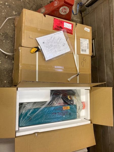 Öppnad fraktlåda med Wegoma matarverk för fräs och installationsmanual ovanpå, i en verkstadsmiljö.