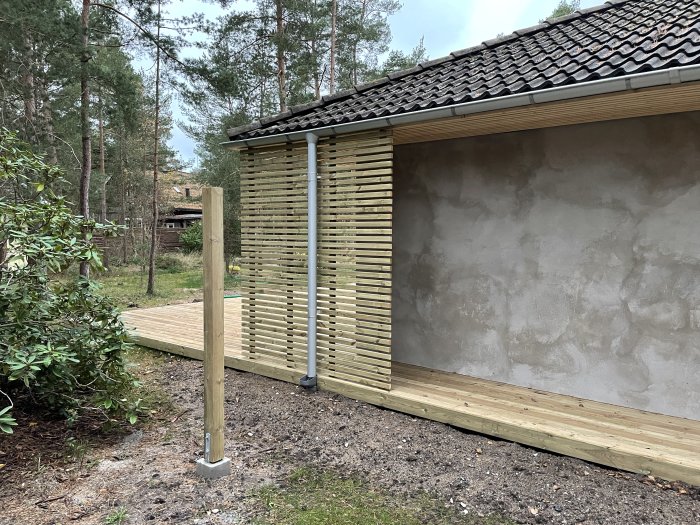 Nybyggd träterrass och putsad fasad på ett hus, omgiven av trädgård och natur.