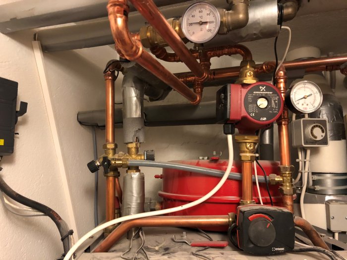 Värmesystem med kopparrör, mätare visar lågt tryck, och en cirkulationspump från Grundfos.