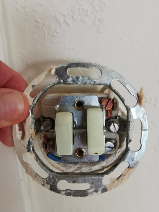 Äldre strömbrytare öppnad i vägg med synliga ledningar och fästelement, i behov av byte.