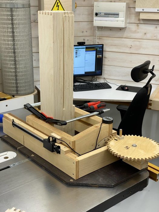 Bordssåg utrustad med en hemmagjord boxjoint-jigg och en exponerad träplanka med fingerfogar stående på sågbordet.