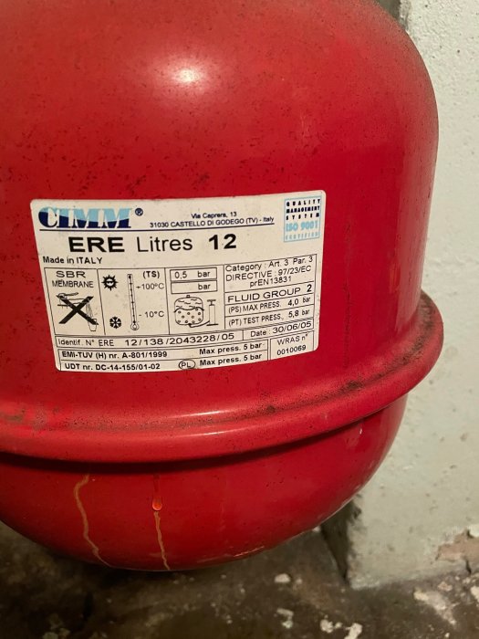 Rött expansionskärl med etikett och tydligt läckage i sömmen på en betongvägg.