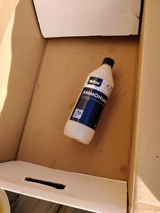 Flaska med ammoniak i en öppen papplåda, enkelt verktyg för träbehandling.