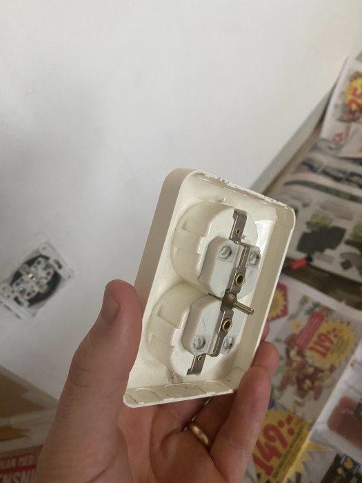 Hand håller en borttagen ljusströmbrytare med en lossad skruv som inte lossnar helt.