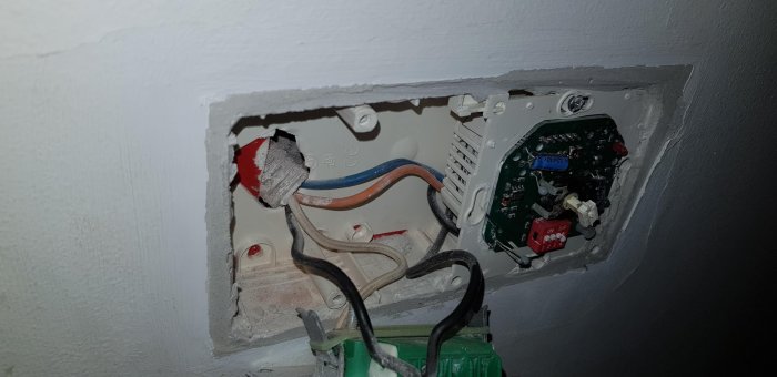 Öppen elektrisk väggdosa med synliga kablar, inklusive potentiella fasledare och termostat.