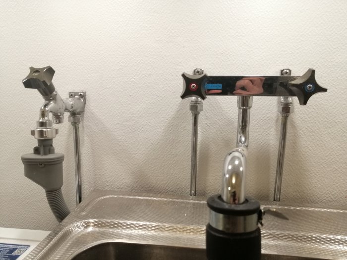 Vattenledningsrör och kranar under diskbänk, kopplade till tvättmaskinskran och diskho.