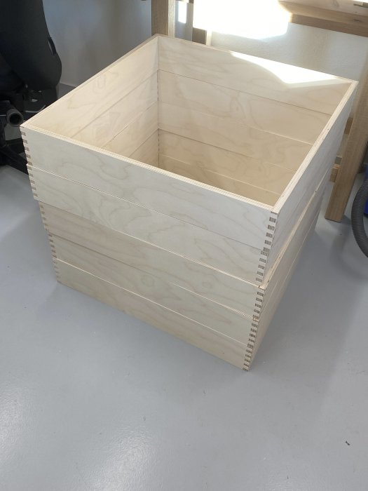 Stor handgjord förvaringslåda i björkplywood med boxjointade hörn utan botten på ett golv.