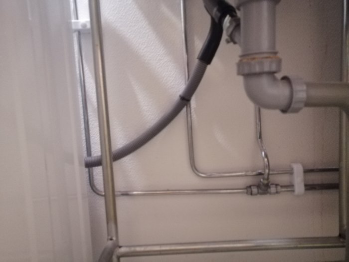 Suddig bild under diskbänk visar rörinstallationer, inklusive kromade och kopparfärgade rör samt avloppsrör.