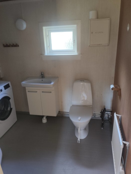 Ett badrum med handfat, toalett, fönster och tvättmaskin, i behov av dekoration ovanför handfatet.