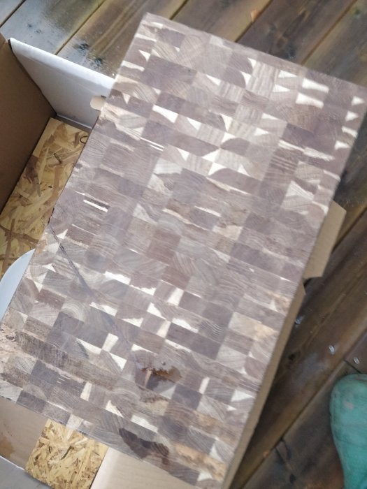 Träskiva med schackbrädemönster ligger utomhus för avluftning innan oljebehandling.