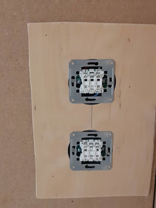 Två installerade eluttag utan frontplattor på en plywoodvägg.