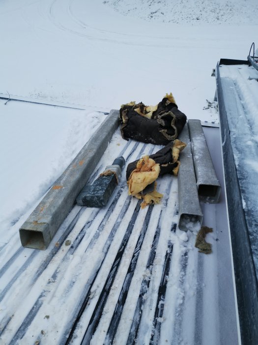 Gammalt isoleringsmaterial och rör ligger på ett snötäckt tak.