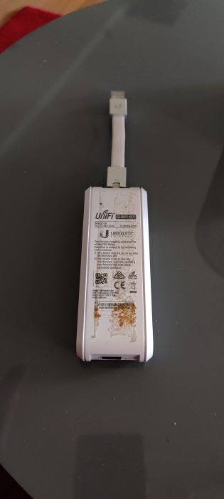 UniFi Cloud Key med USB-kabel och spår av dubbelhäftande tejp på baksidan.