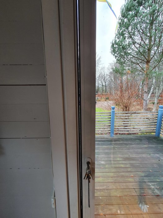 Öppet Schuko vikdörrsparti i en stuga som visar en otätning och ett nyckelknippe i dörren med utsikt mot en trädgård.