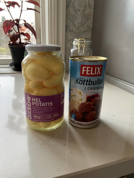 Burk med hel potatis och en konservburk med köttbullar i gräddsås på ett köksbord.