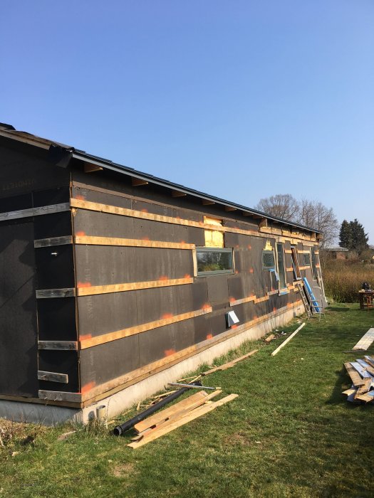 Hus under renovering med delvis saknad fasad och exponerade väggpartier, material spridda på marken.