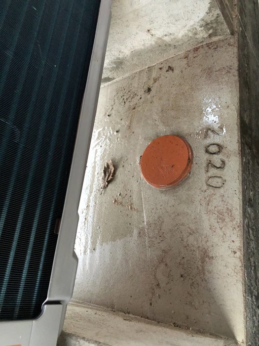 Bild på ett nyligen gjutet fundament med ett orange täcklock över en muffända bredvid en värmepumps utedel.