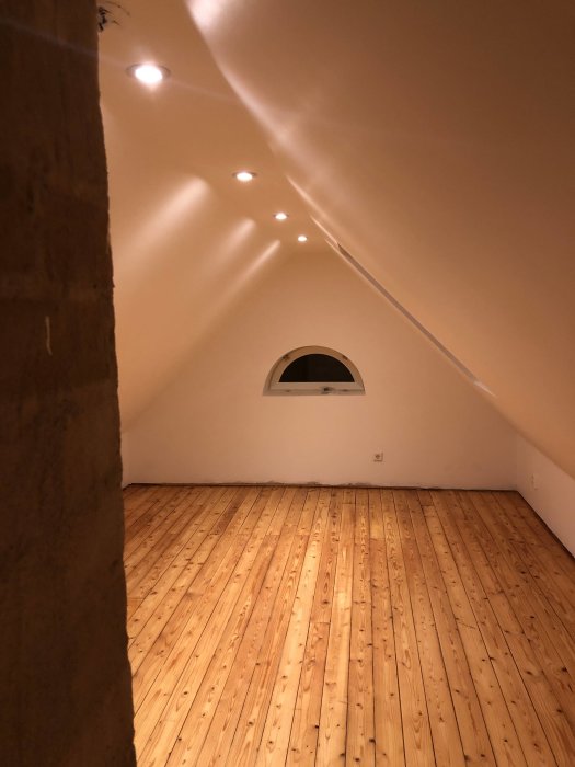 Renoverat rum med snedtak och inbyggda spotlights, trägolv och en rundad övergång till taket.