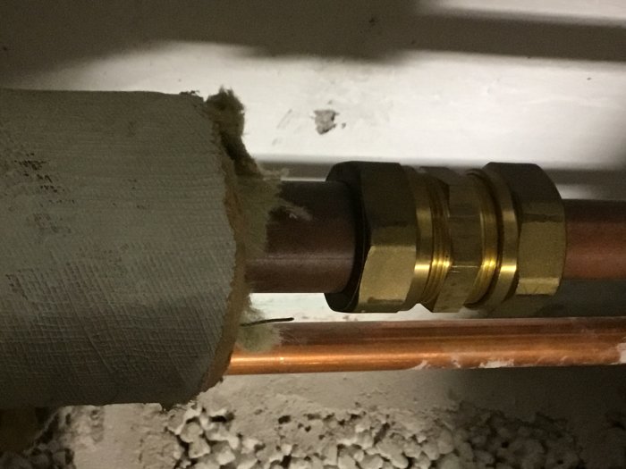 Kopparvattenrör ansluten till en guldaktig Conex T-koppling, omgiven av isolering och väggelement.