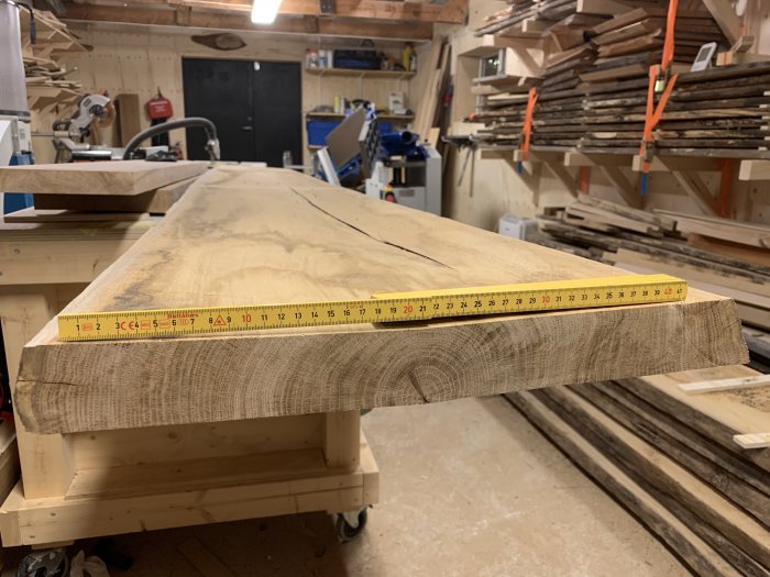 Trämåttband ligger på en grovt tillhuggen träplanka i en snickarverkstad.