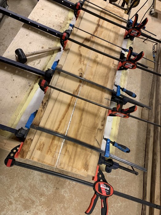 Träplankor limmas ihop till en bänkskiva med klämmor i en verkstad.