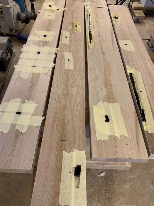 Olika träplankor i en verkstad, några med epoxylagning, grovkapade och andra i limningsprocess.