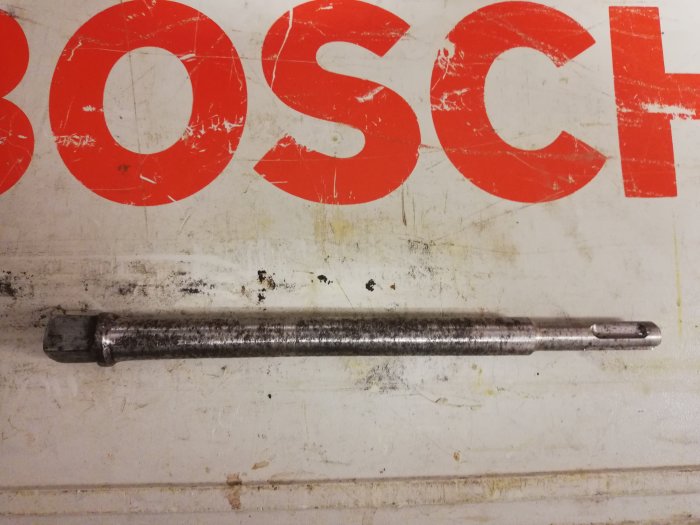Modifierad förlängare för verktyg framställd med svarv och fräsmaskiner, ligger på en sliten Bosch-skylt.