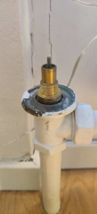 Radiatortopp utan vred med synlig metallpinne och gängad anslutning mot en vit vägg och trägolv.