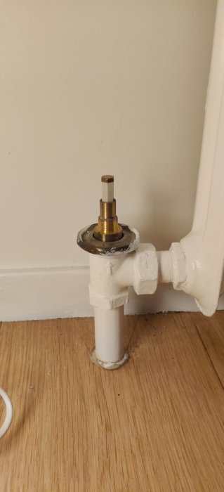 Radiatorkoppel utan vred, en plastpinne och metallpinne sticker upp mot en vit vägg.