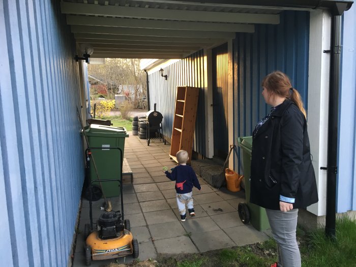 Nyckelöverlämning dag, kvinna och barn på gångväg med bråte, trädgårdsavfall och en gammal gräsklippare utanför huset.