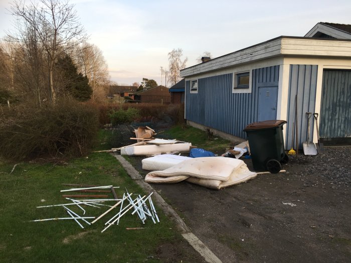 Trädgård med skräp och gamla möbler utanför ett blått hus, dagen för fastighetsövertagande.