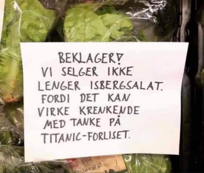 Lapp med texten "Beklager! Vi selger ikke lenger isbergsalat fordi det kan virke krenkende med tanke på Titanic-forliset" framför salladsblad.