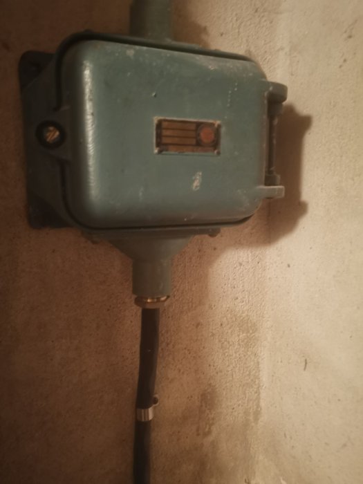 Äldre grå elcentral uppsatt på en betongvägg med elledning kopplad, troligen innehållandes huvudsäkringar.