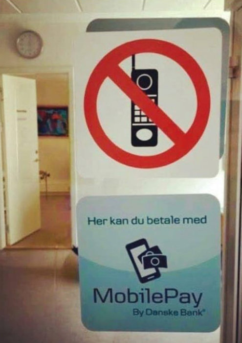 Skylt med mobilförbud ovan och MobilePay-betalningsalternativ nedan, inomhus.