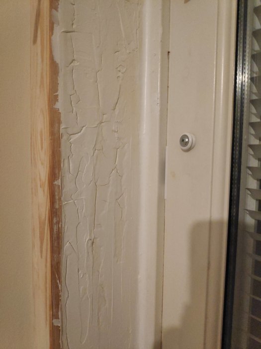 Fönsterkarm med spruckna spackellager vid renovering, nära ett fönster med byggfog.