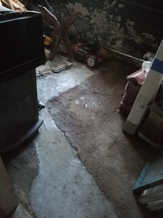 Fuktig källare med synliga vattenskador, saker förvarade och grävd skyttegrav i betonggolv.