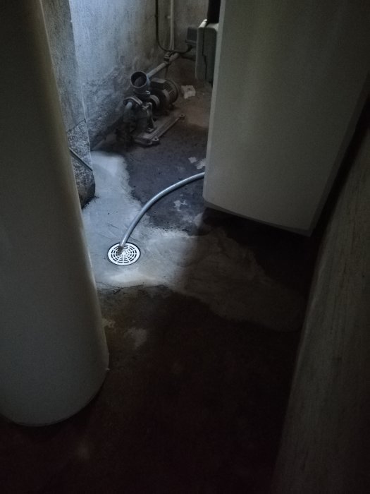 Källare med synlig fukt på betonggolvet och en pumpbrunn med avloppsrör.