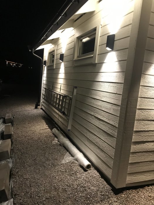 Exteriör av hus vid natt med spotlights och omonterade rör på marken som förberedelse för elinstallation.