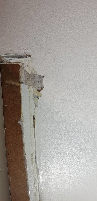 Vägg med skarv där gammal tapet möter nymålad spacklad yta och masonitskiva.